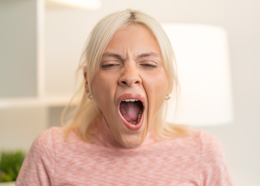 A young, blonde woman wearing a pink sweater lets out a giant yawn of boredom
