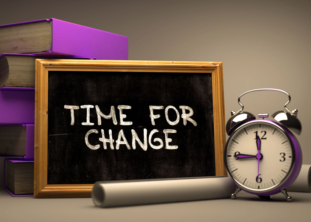 An image of a clock and a stack of books with a chalkboard in front that says "time for change"