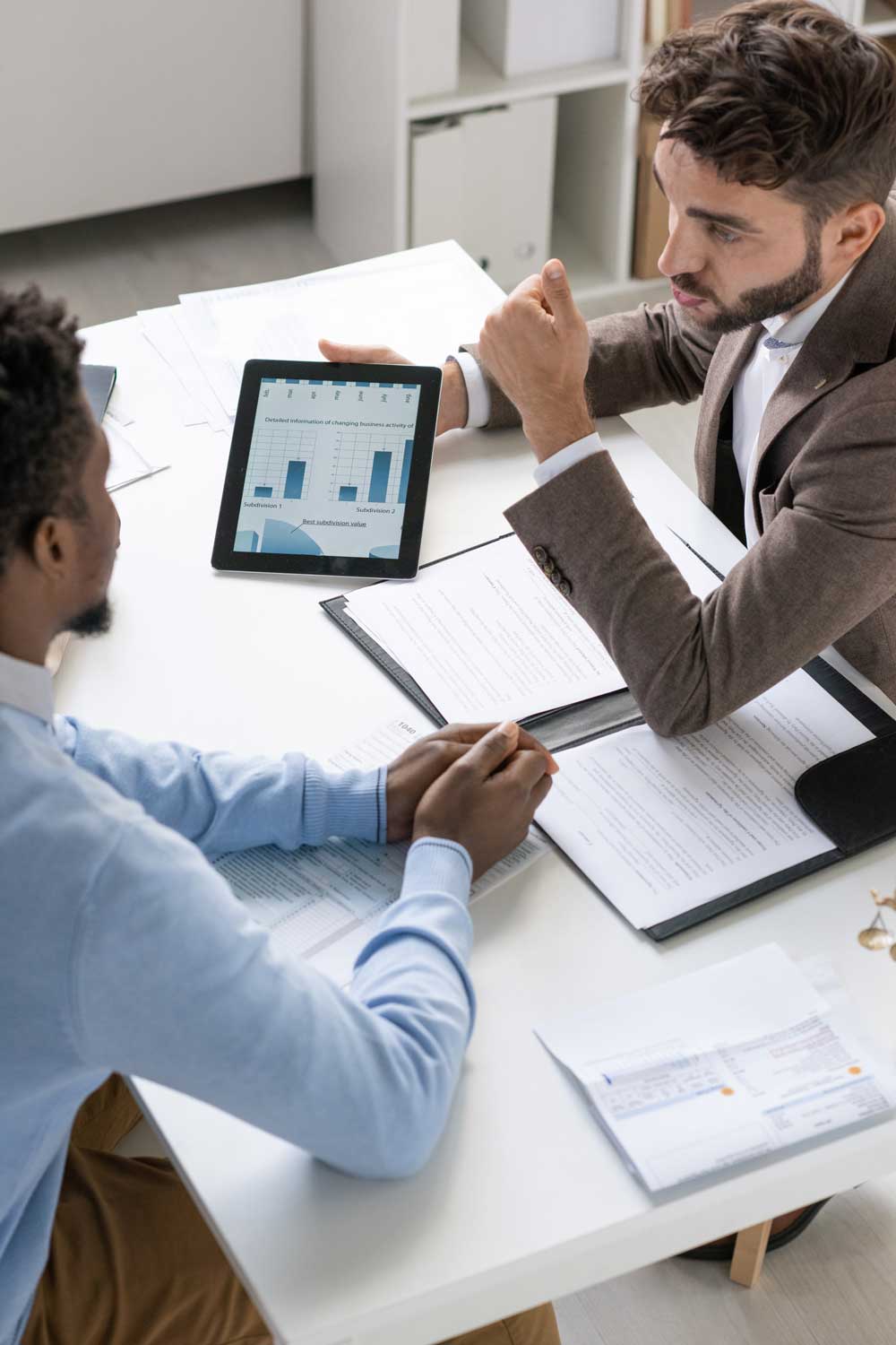 Two men discuss reports while looking at investment documents